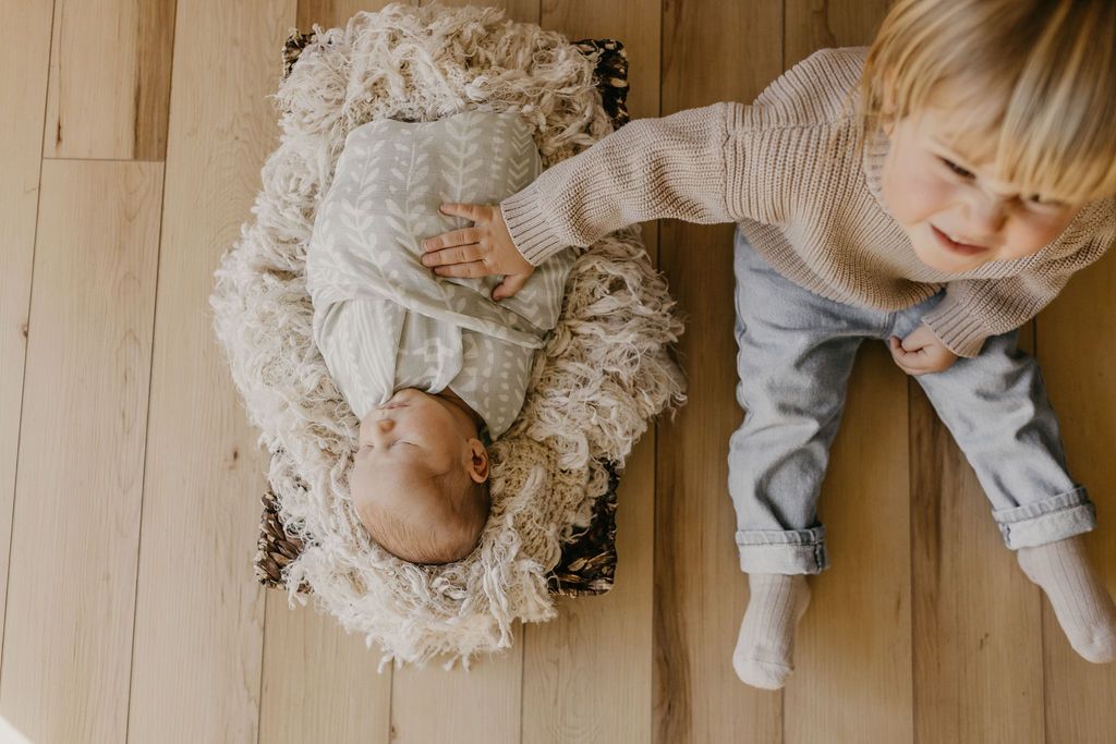 things to do with a newborn, baby boy swaddled in a basket with an older sibling next to him