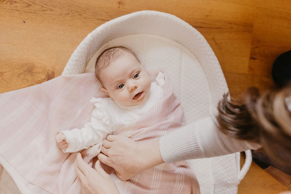 newborn baby girl being swaddled in a rose mauve stripe swaddling cloth