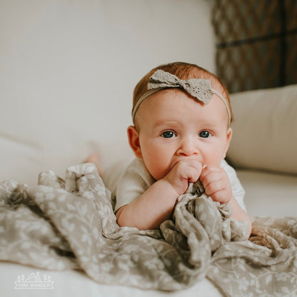 a close up photo of a baby girl sleeping soundly wrapped in her light weight and breathable floral gray baby blanket muslin swaddle wrap