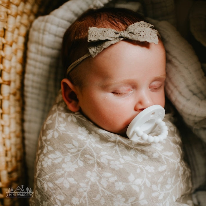 a close up photo of a baby girl sleeping soundly wrapped in her light weight and breathable floral gray baby blanket muslin swaddle wrap