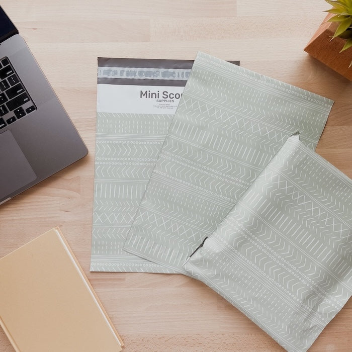 three poly mailers in the sage green or pastel green color laid flat on the wooden desk