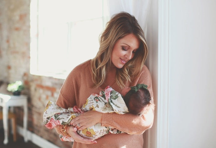 A mama is holding her sleeping baby daughter. The baby girl is wrapped in a flowery cotton blanket.