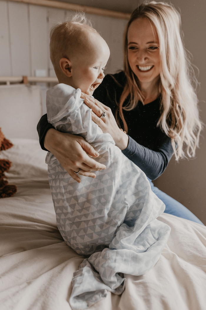 mom is grinning while looking at her baby wrapped in a blue swaddle blanket