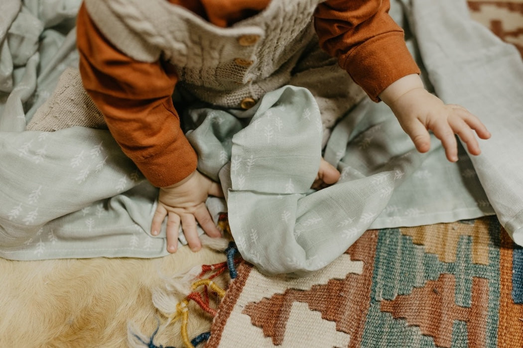 photo of a baby crawling showing just the hands, arms and body wearing earth tone clothes looking like babys first christmas with christmas decors and babys first christmas gifts