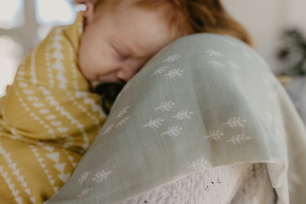 baby boy resting and sleeping over mom's shoulders using the baby muslin blanket as cover and a baby boy lovey