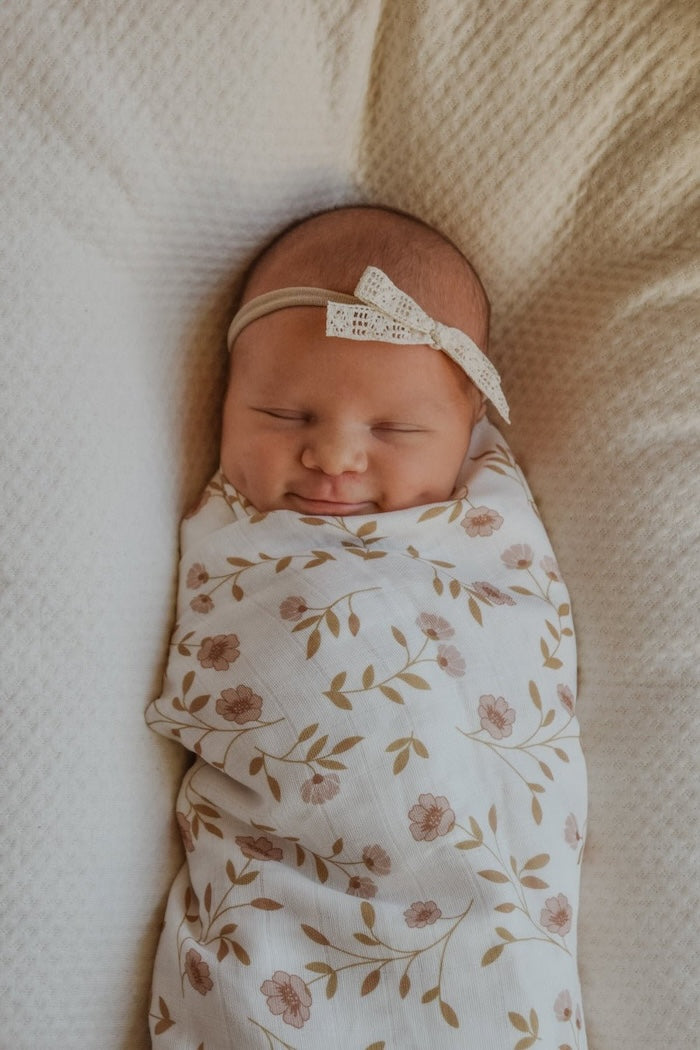 a cute baby wrapped in our wildflowers pink floral baby blanket wearing a white ribbon headband smiling showing her dimples