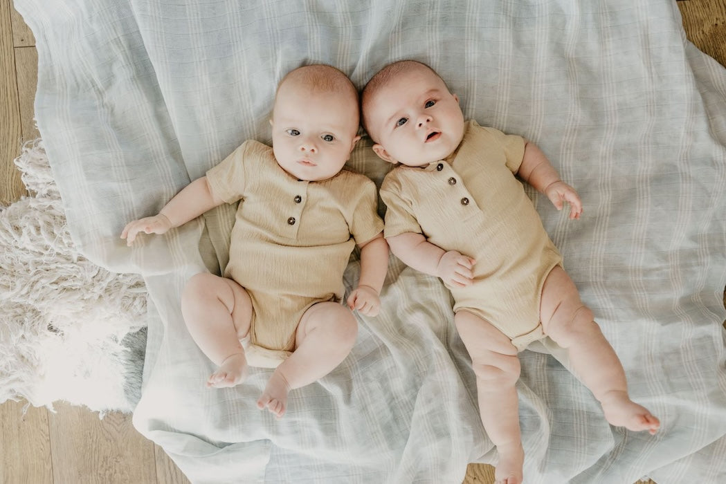 two cute babies lying flat in their backs, with the stripe baby swaddle as bed cover looking curiously at the camera