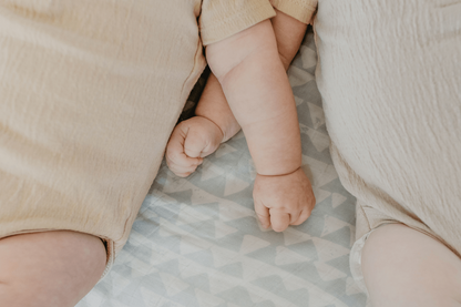 babies wearing neutral colored baby clothes lying on top of the blue swaddle blanket arms are crossed