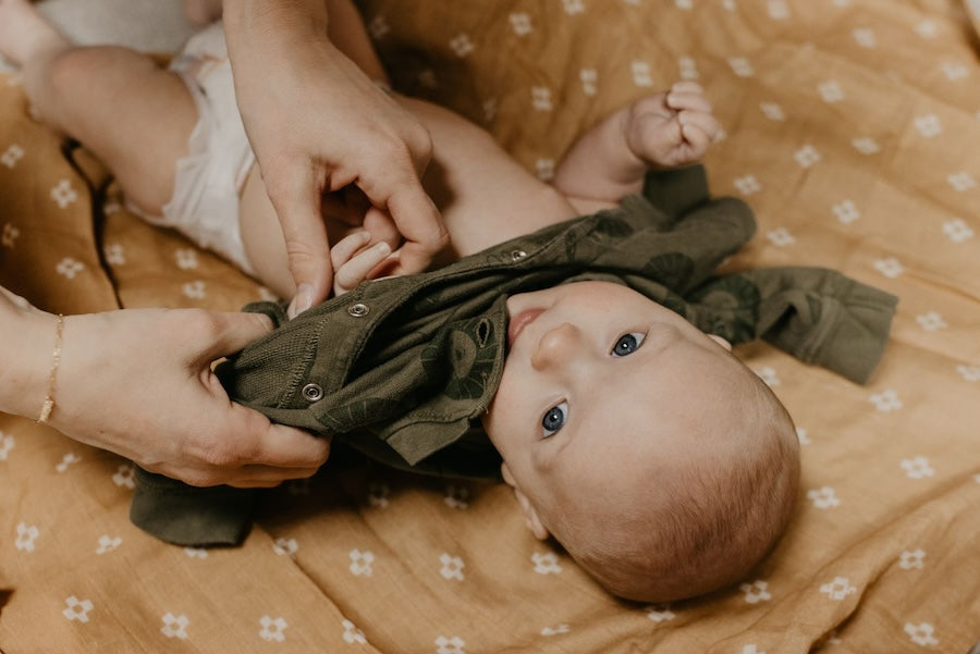 the brown muslin swaddle blanket used as a changing pad cover showing mom and baby changing baby's clothes