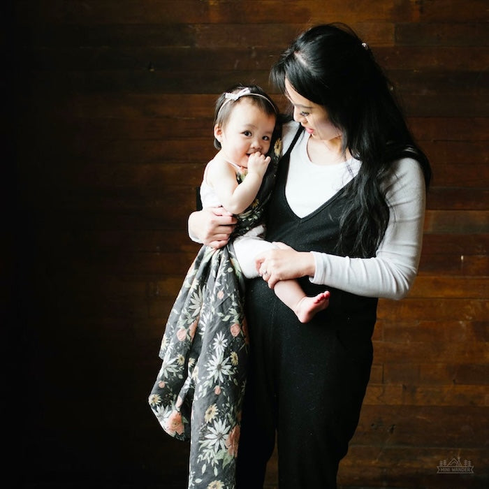 a beautiful photo of mom carrying her her child wearing boho baby clothes with the charcoal gray cotton swaddle slightly wrapped around the baby's body