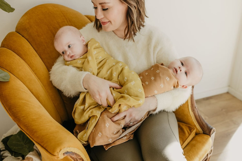 mommy and her twin babies sitting in an accent chair with babies wrapped in a muslin swaddle baby blanket