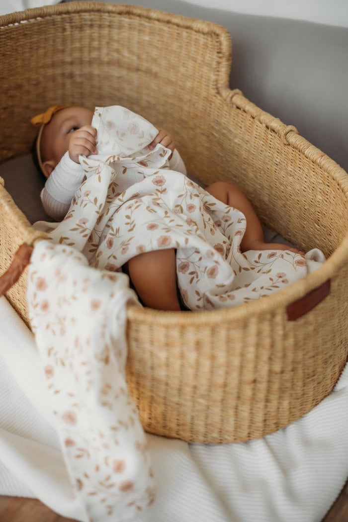 an adorable baby lying in her baby bassinet wearing cute baby clothes holding the wildflower white floral baby blanket