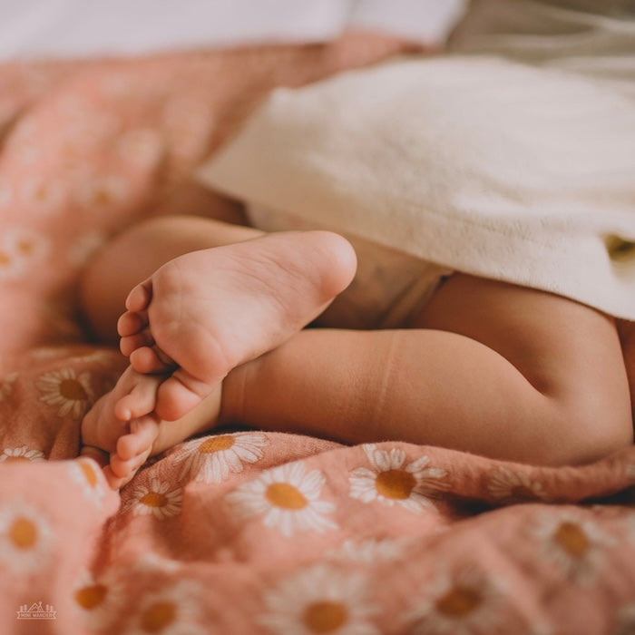 A baby on his tummy was laid in a pink daisy swaddle.