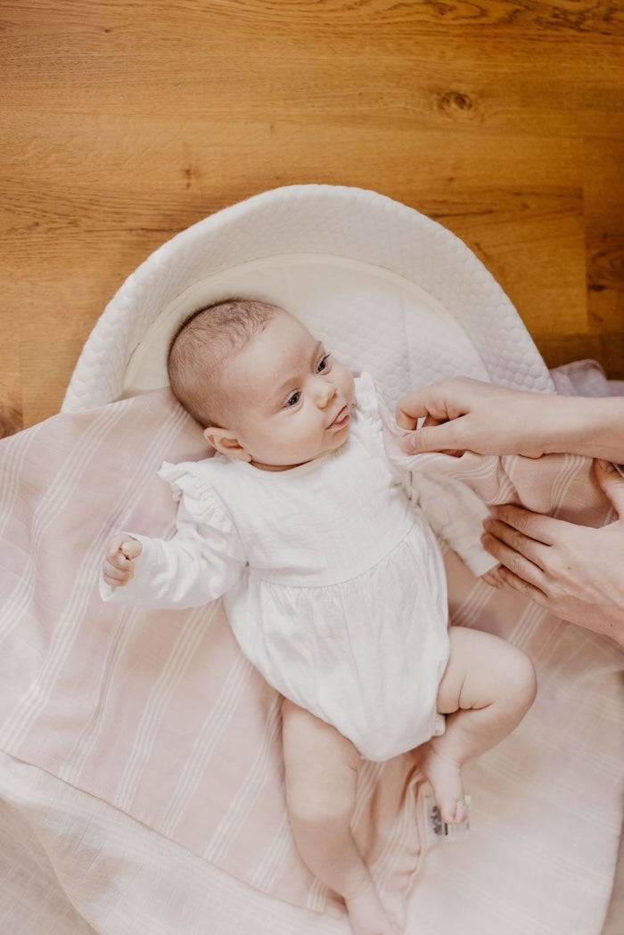 baby with tongue out in her changing pad being changed by mom using their favorite baby item which is our classic stripe blankets in smoky rose mauve color