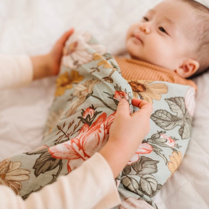 Big sis is swaddling the sleepy baby in her mini wander garden floral swaddle.