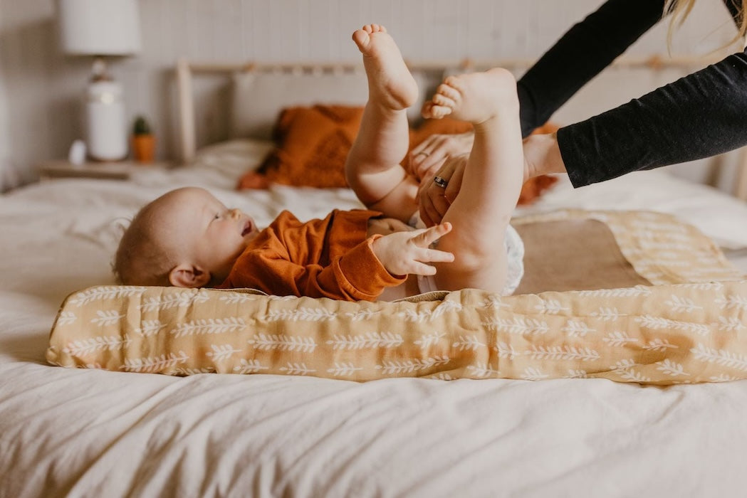 cutest photo of mom and a happy baby where mom changes the baby's diaper while using the cream baby blanket as a changing pad cover