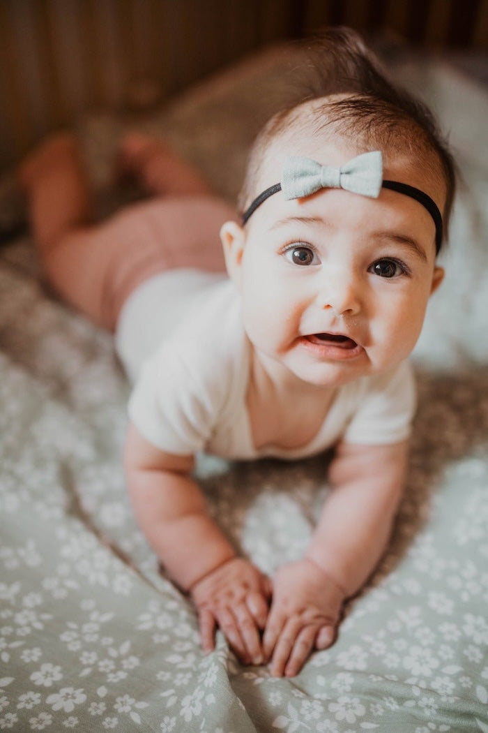 A baby in a sage green with white floral swaddle with a white ribbon on her head.
