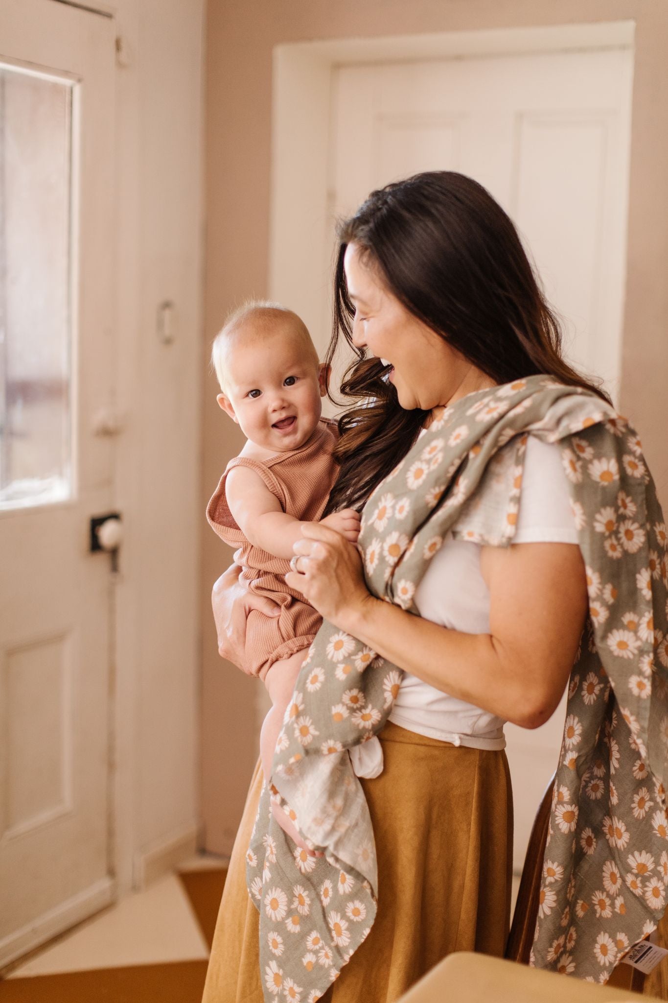 mama holding a baby and using a daisy green baby blanket as a burp cloth