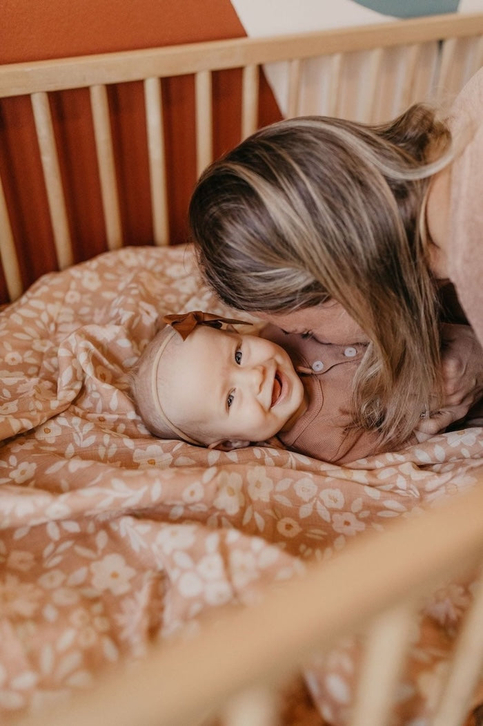 mommy kissing happy baby in her crib lined with the best baby essentials which is the meadow dessert cute baby stuff