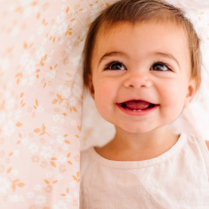 A cute smiling baby hoods up on a peach swaddle with small daisies.