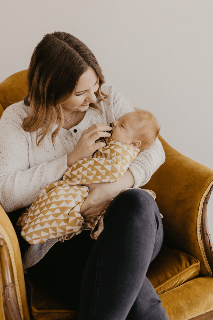 mommy carrying her sleeping baby in her arms swaddled in our mountain swaddle in honeygold color