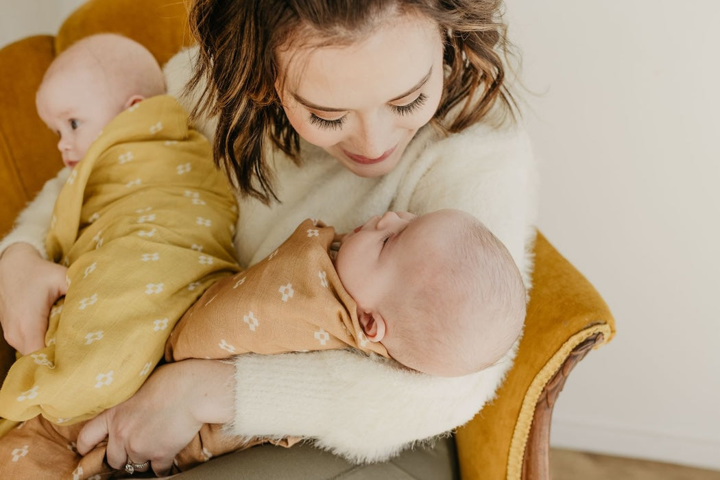 smiling mommy holding her twin babies that are wrapped in a muslin swaddle baby blanket