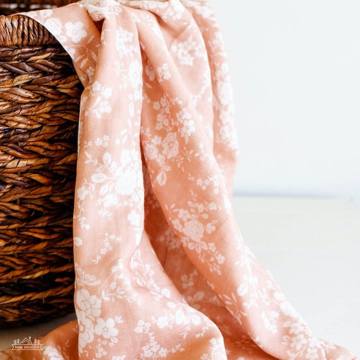 peach vintage bouquet floral muslin swaddle hanging on the side of the wooden basket