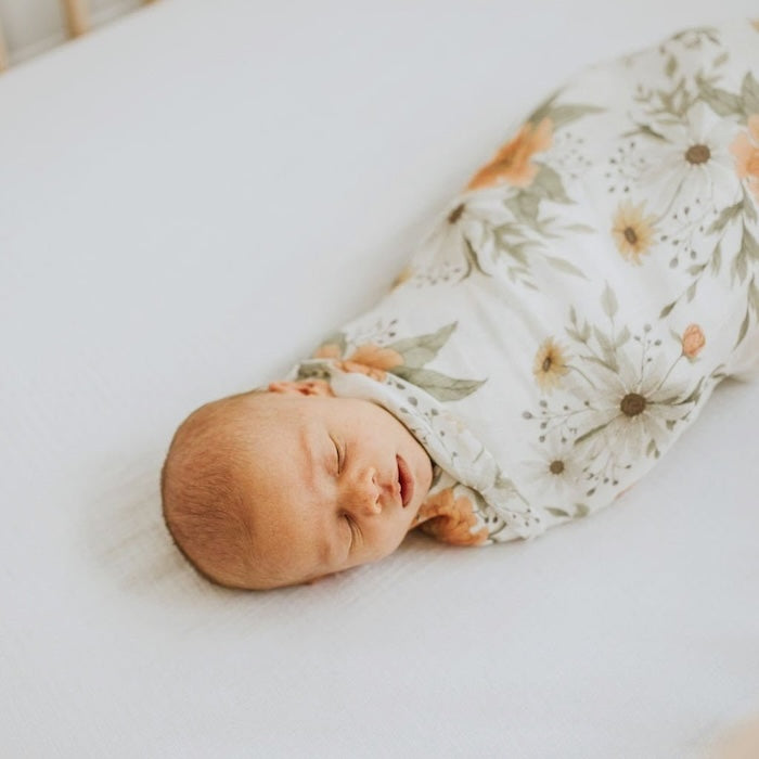 little one sleeping snug as a bug carefully wrapped in The Mini Wander Spring Blossom white peony baby swaddle