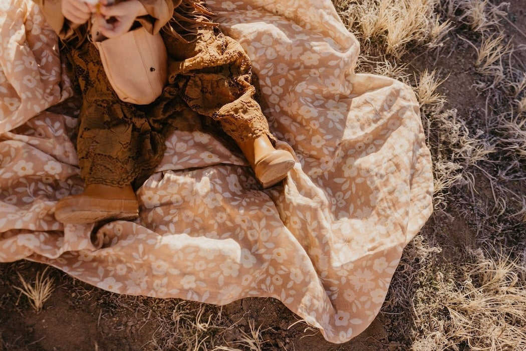 photo of a baby sitting on the best baby wrap showing the hem of her brown dress and her brown boots with some cute baby stuff