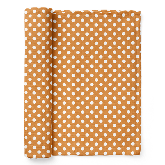 half rolled polka dot swaddle blanket in white dots over an amber color background