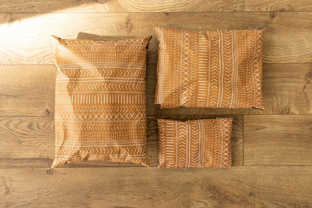 A photo comparing different sized poly mailers. Brown color with white block printed boho line design. Pictured are sizes 12x15.5 , 10x13 and 6x9 self sealing plastic shipping envelopes.