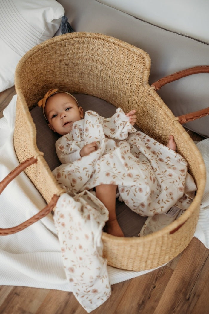 a cuddly baby girl wearing cute baby clothes lying in her baby basket using her floral baby blanket as a blanket for baby