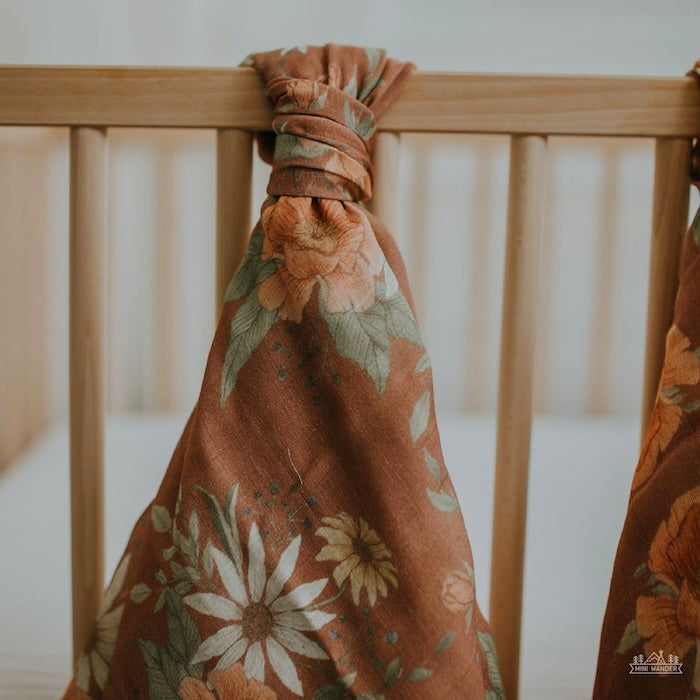 photo of our spring blossom clay muslin baby swaddles tied nicely on top of the wooden crib in a boho nursery setting