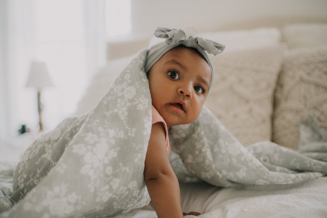 sweet baby girl crawling under the vintage bouquet geen swaddle looking at the camera