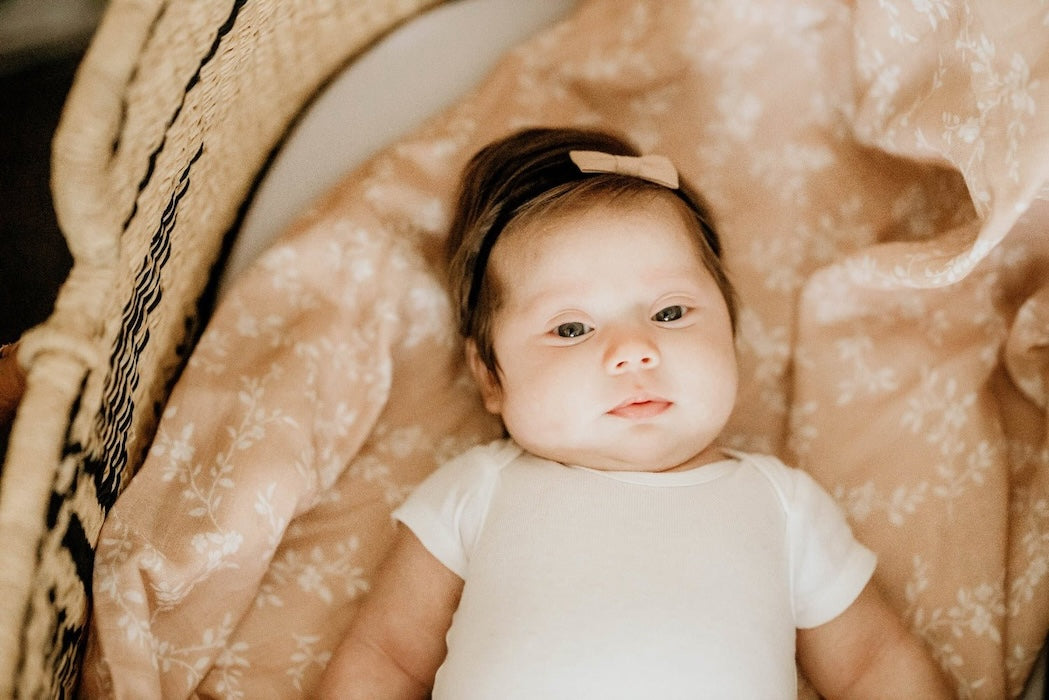 little baby wearing a pink dainty ribbon and white baby clothes lounging comfortably in her peach summer blanket