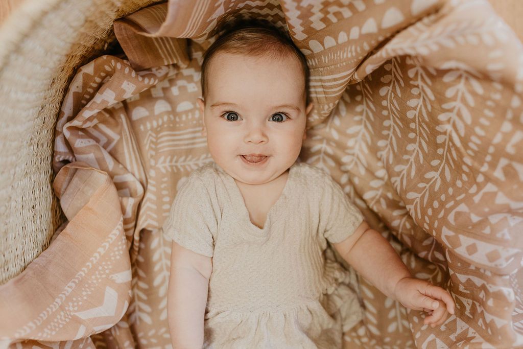 baby girl smiling beautifully infront of the camera lying on top of the tapestry swaddle blanket one of the baby gift set for girls
