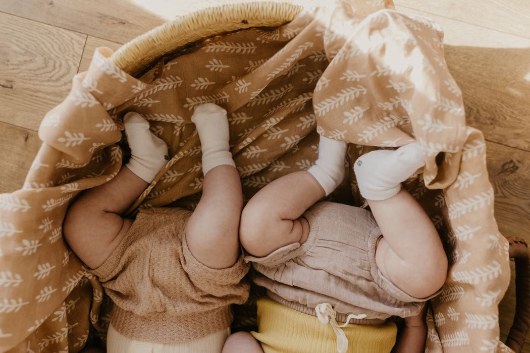 an upside down image of two baby thigh and feet in a baby bassinet lined and covered with the wheat muslin blankets