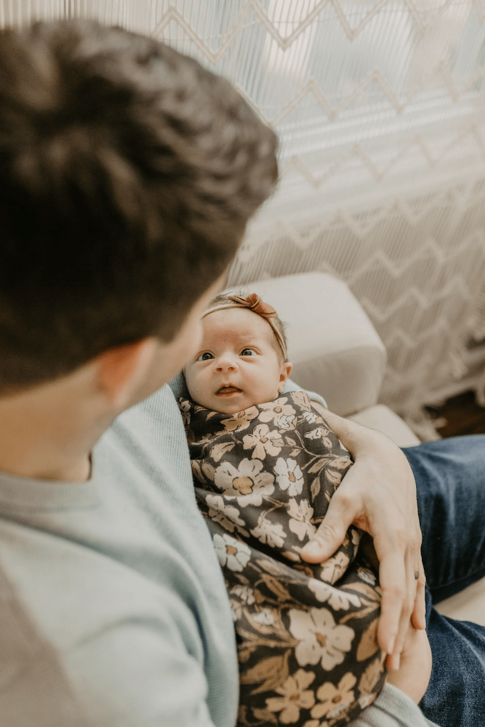 a beautiful photo of baby wrapped in our gorgeous thicket flower swaddle looking at her dad with so much love and affection