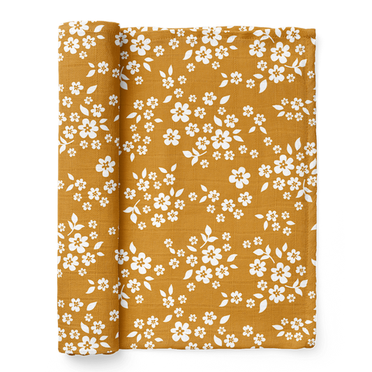 A half-rolled Mini Wander swaddle with a rich, yellow, and whimsical Floral design.