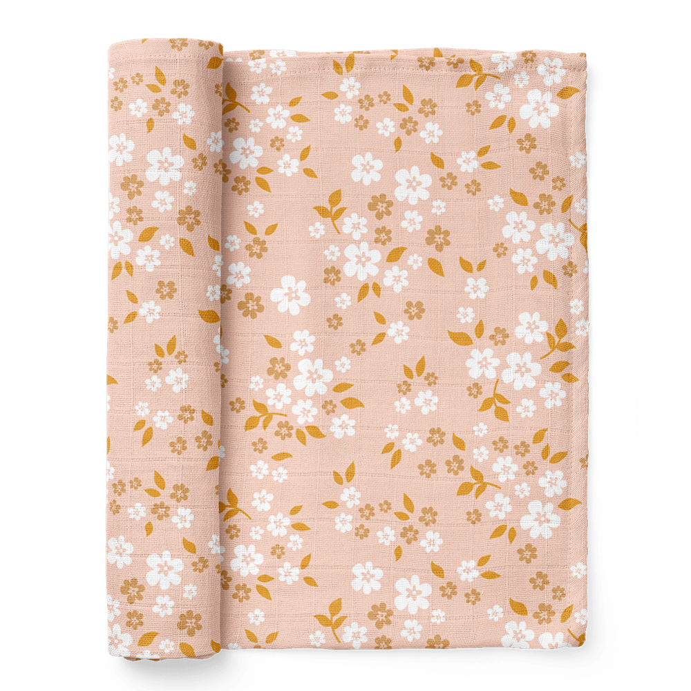 A half-rolled Mini Wander swaddle blanket peppered with daisies and delicate leaves design on a floral peach background.