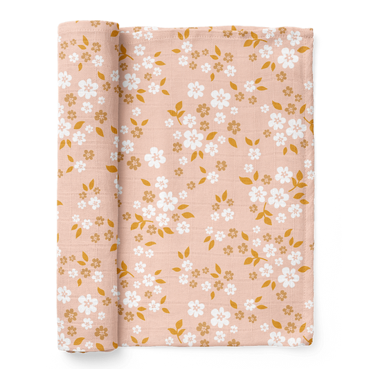 A half-rolled Mini Wander swaddle blanket peppered with daisies and delicate leaves design on a floral peach background.