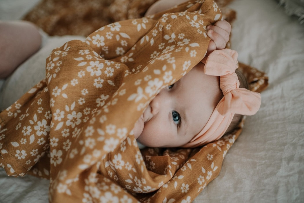 peekaboo baby in the mustard yellow baby floral blanket which is part of the baby gift set for girls