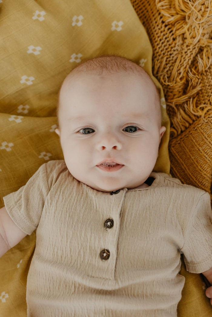 baby boy smiling at the camera wearing gender neutral baby clothes lying on a yellow baby blanket