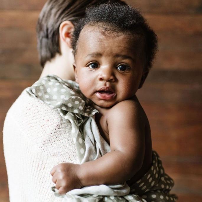 baby boy held by the mom on her shoulders with the green polka dot swaddle blanket as a wrap and a cover