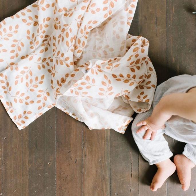The leaves Amber swaddle baby boy gifts blanket placed on the floor with the photo of a baby's half body showing sitting on the wooden floor