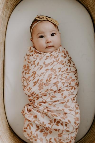 cute photo of an adorable baby girl looking at the camera wrapped in her brown floral muslin blanket
