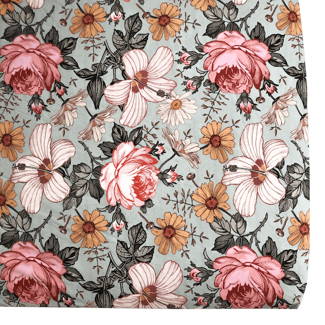 A close up of Mini Wander cribsheet with a floral design on a green background. Flowers printed on the cribsheet include daisies, roses, and a creamy pink hibiscus.