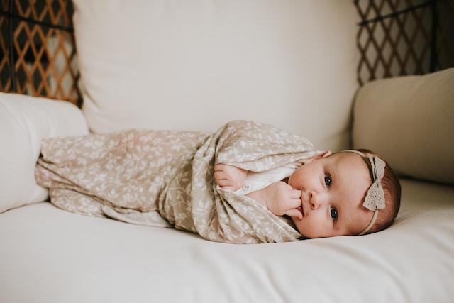 sweetest baby girl biting her two tiny fingers and laying on her side on her comfy chair wrapped in her floral gray baby blanket in the magnolia tree print