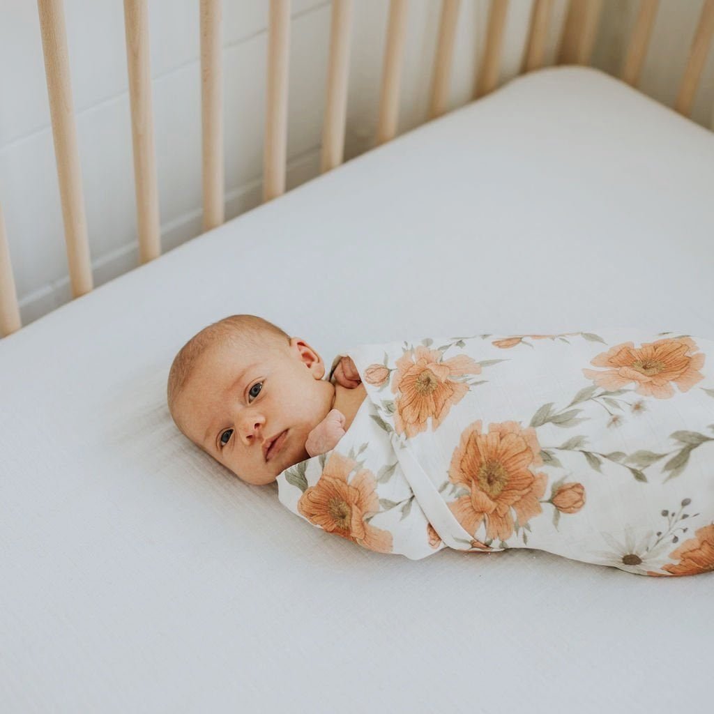 adorable baby swaddled in a beautiful floral peony swaddle lying in her wooden crib