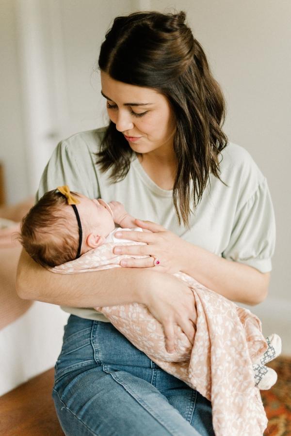 mom and baby sweet moment showing mom holding her sleeping baby in her arms while the baby is wrapped in her peach pink swaddle blanket